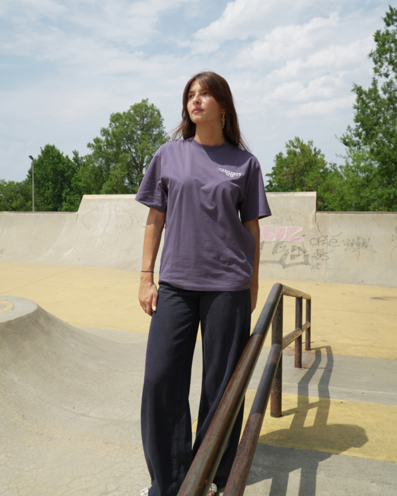 Femme portant un t-shirt violet et un pantalon noir de la marque Carhartt.
