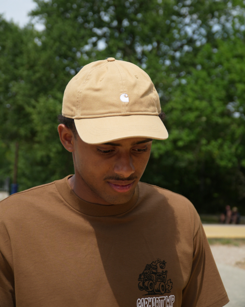 Homme portant une casquette beige et un t-shirt marron de la marque Carhartt Wip